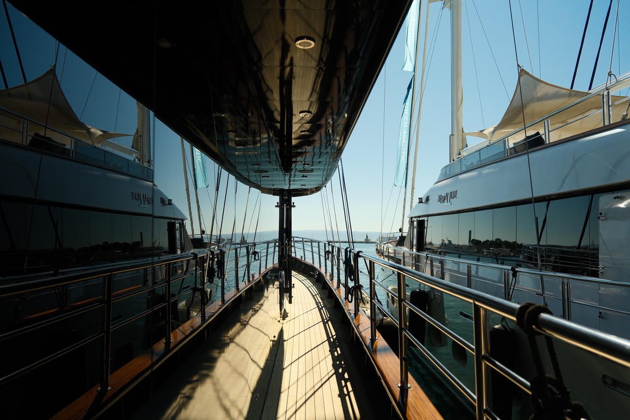 Seitendeck zwischen zwei Superyachten im Hafen, die Rümpfe spiegeln Himmel und Wasser