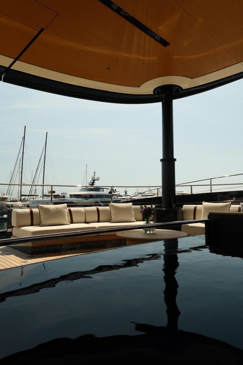 Lounge unter einem Holzdach an Deck, davor ein dunkler Pool mit Spiegelung