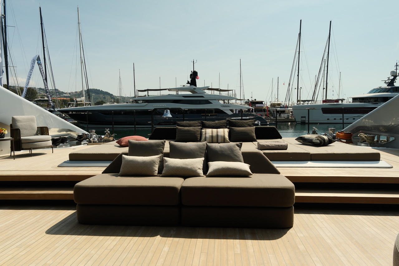 Großzügiges Sofa an Deck einer Superyacht, dahinter ein Hafen mit Yachten