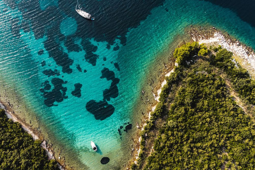 Türkisfarbene Bucht in Süddalmatien von oben, darin eine Segelyacht und ein Motorboot